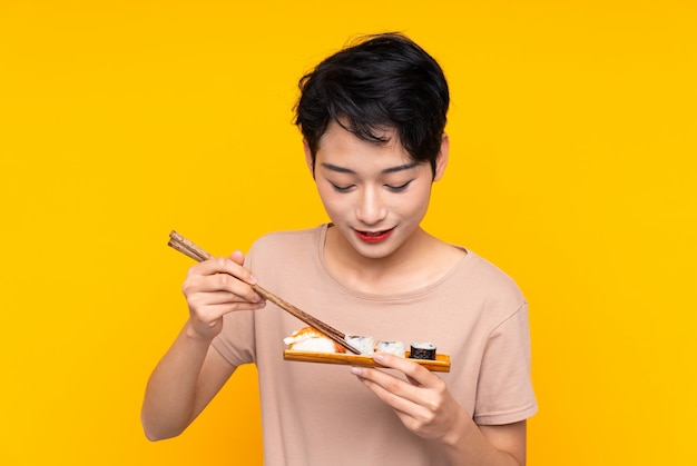 Giovane donna asiatica con i sushi sopra la parete gialla