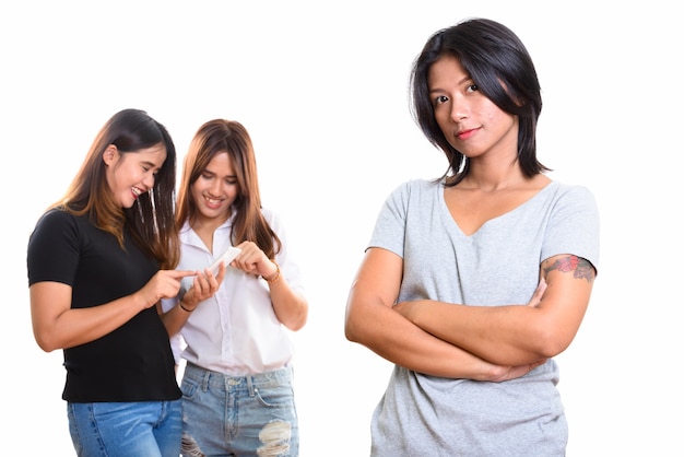 Giovane donna asiatica con le braccia incrociate con due amici felici sul retro utilizzando il telefono cellulare insieme