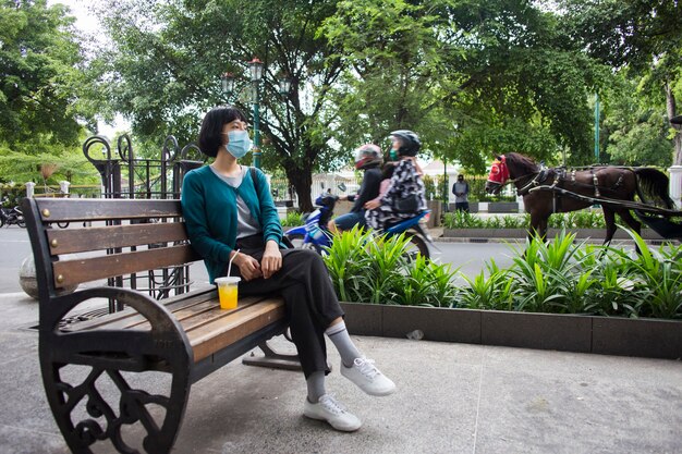 Giovane donna asiatica con maschera facciale seduta in spazi pubblici Concetto del virus Corona