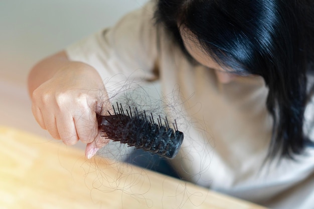 Giovane donna asiatica con pettine e capelli problematici su sfondo beige chiaro