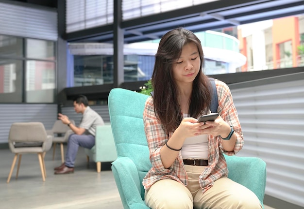 Giovane donna asiatica con un uomo dietro di lei che usa il cellulare per inviare messaggi di testo o leggere online