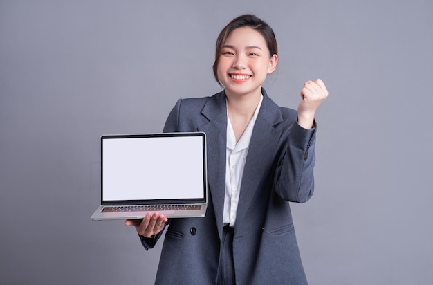 Giovane donna asiatica d'affari che indossa un abito e utilizza il computer portatile su baclground grigio