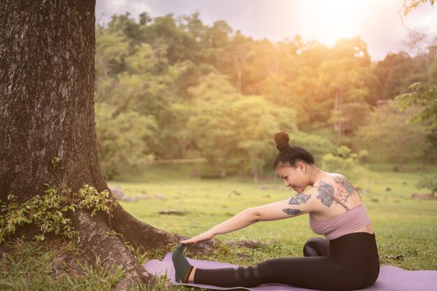 Giovane donna asiatica del tatuaggio che fa yoga nel parco