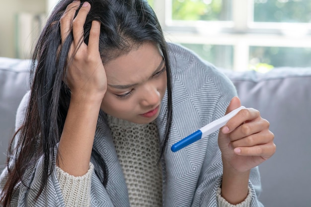 Giovane donna asiatica depressa che tiene un test di gravidanza negativo o positivo