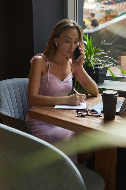 Giovane donna asiatica di affari che scrive note in taccuino al caffè che lavora al computer portatile