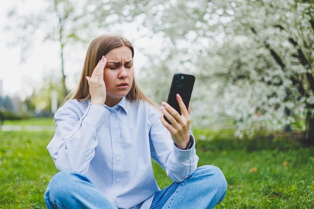 Giovane donna asiatica emotiva che usa il telefono cellulare guardando le notizie di allevamento online di video seduti sull'erba Shopping femminile eccitato online