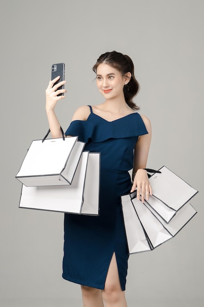 Giovane donna asiatica energica che tiene il telefono cellulare in bianco dello schermo con le borse della spesa su fondo grigio
