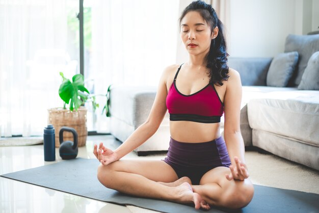 Giovane donna asiatica esercizio di yoga a casa palestra, stile di vita femminile sano con allenamento sportivo fitness a casa, ragazza che fa esercizio fisico attivo per il corpo sala interna casa, relax e benessere