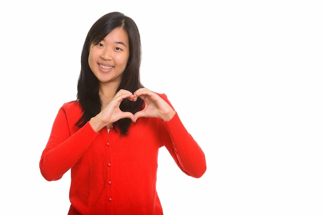 Giovane donna asiatica felice che dà il segno del cuore isolato