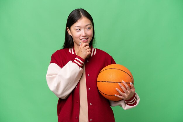 Giovane donna asiatica giocatore di basket su sfondo isolato guardando al lato e sorridente