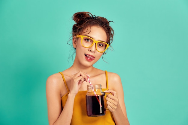 Giovane donna asiatica in abiti casual che tiene una tazza di soda sopra l'azzurro