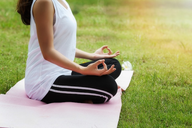 Giovane donna asiatica in abiti sportivi che meditating mentre sedendosi nella posa del loto sulla stuoia di yoga