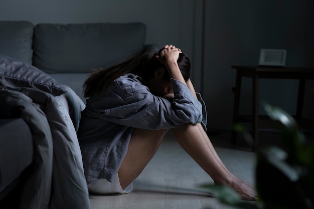 Giovane donna asiatica in camera da letto che si sente triste, stanca e preoccupata che soffre di depressione nella salute mentale