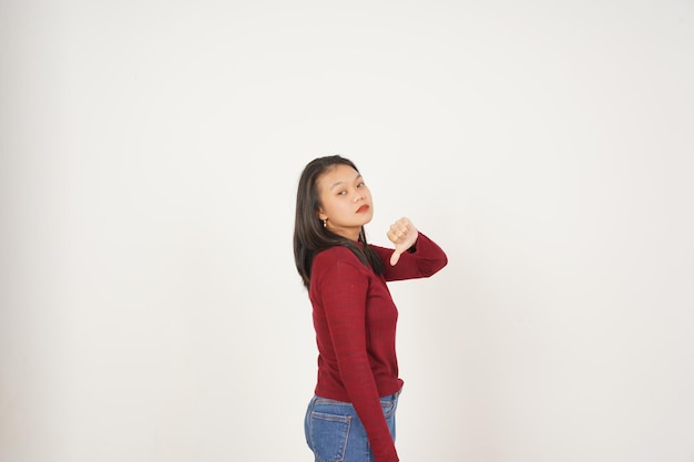 Giovane donna asiatica in maglietta rossa che mostra il pollice verso il basso non è d'accordo con il concetto isolato su uno sfondo bianco
