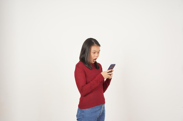 Giovane donna asiatica in maglietta rossa wow scioccata mentre usa lo smartphone isolato su sfondo bianco