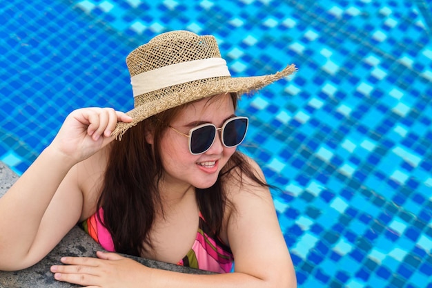 Giovane donna asiatica in sovrappeso che indossa un costume da bagno arancione e un cappello da sole sulla spiaggia di paglia che si rilassa in piscina Felice donna taglie forti allegra divertente vacanza in viaggio d'estate