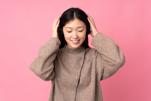 Giovane donna asiatica isolata su musica d'ascolto della parete rosa