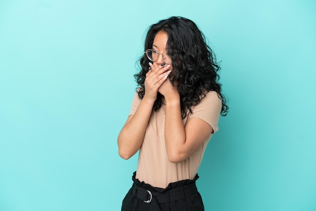 Giovane donna asiatica isolata su sfondo blu che copre la bocca e guarda di lato