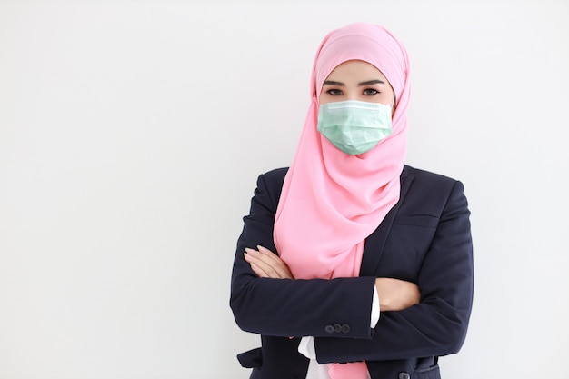 Giovane donna asiatica musulmana graziosa e sicura che indossa vestito blu con la maschera protettiva medica per proteggere l'infezione da Coronavirus in studio sul ritratto isolato del fondo bianco