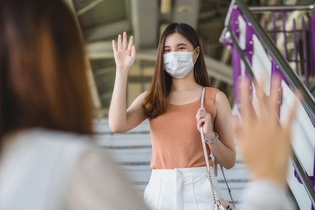 Giovane donna asiatica passeggero che indossa una maschera chirurgica e agita la mano per salutare