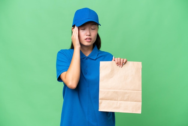 Giovane donna asiatica prendendo un sacchetto di cibo da asporto su sfondo isolato con mal di testa