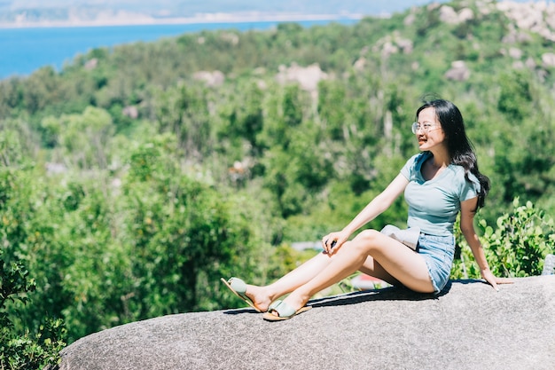 Giovane donna asiatica seduta su una roccia in estate