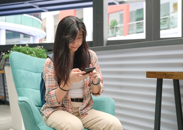 Giovane donna asiatica seduta sulla sedia e guardando il cellulare