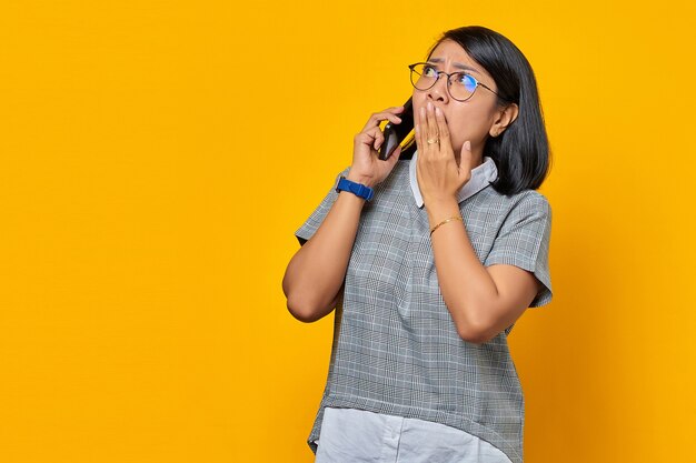 Giovane donna asiatica sorpresa nel ricevere una chiamata in arrivo sul telefono cellulare e nel coprire la bocca con la mano