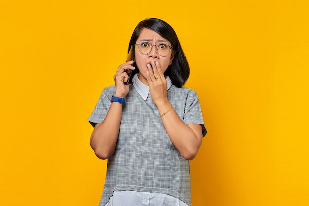 Giovane donna asiatica sorpresa nel ricevere una chiamata in arrivo sul telefono cellulare e nel coprire la bocca con la mano