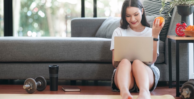 Giovane donna asiatica sorridente che per mezzo del computer portatile mentre restano a casa.