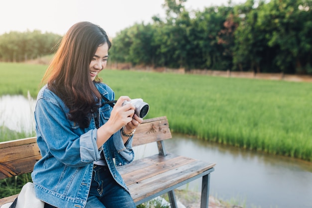 Giovane donna asiatica sorridente. Ragazza che usando la macchina fotografica e godendo alla bella natura con il tramonto.