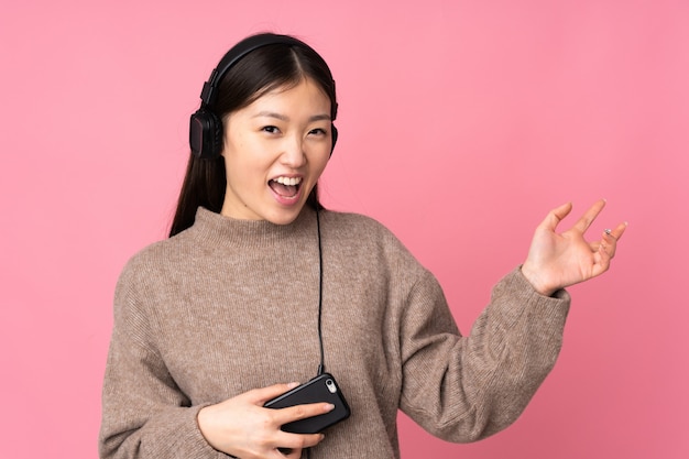 Giovane donna asiatica su musica d'ascolto della parete rosa e fare il gesto della chitarra