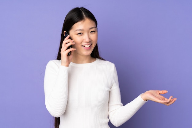 Giovane donna asiatica sulla parete viola mantenendo una conversazione con il telefono cellulare con qualcuno