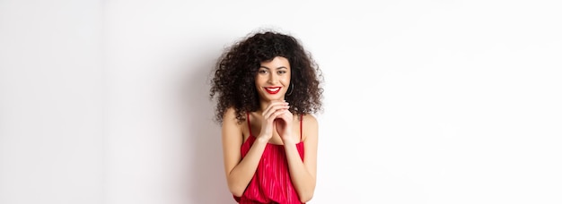 Giovane donna astuta con le dita del campanile dei capelli ricci e il sorriso subdolo con un piano in piedi in re