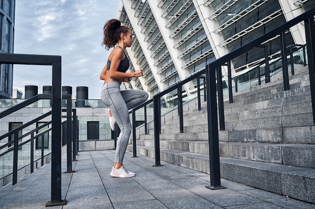 Giovane donna atletica che corre al piano di sopra saltando l'allenamento allo stadio urbano della città