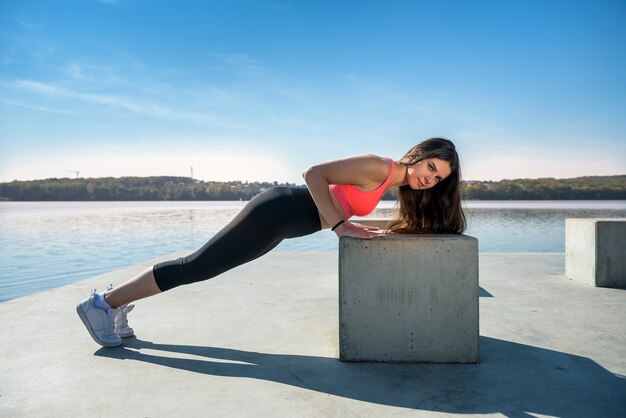 Giovane donna atletica che fa flessioni. Ragazza che fa esercizi di fitness vicino al lago durante il giorno