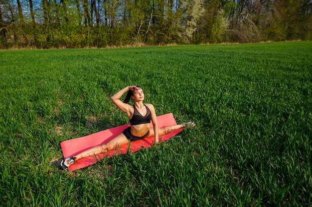 Giovane donna atletica che fa spaccature longitudinali all'aperto. La ragazza pratica sport, stile di vita sano, corpo atletico. Indossa abbigliamento sportivo, top nero e pantaloncini. concetto di sport.