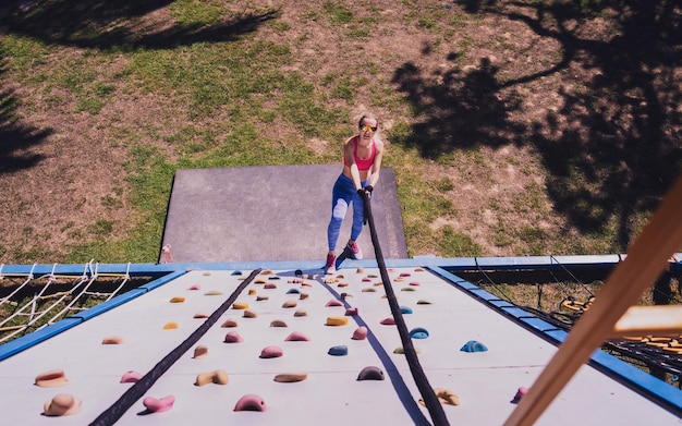 Giovane donna atletica che si allena e si arrampica su una corda al campo di addestramento della corda