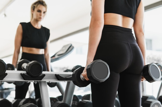 Giovane donna atletica durante il suo allenamento fitness con manubri in palestra