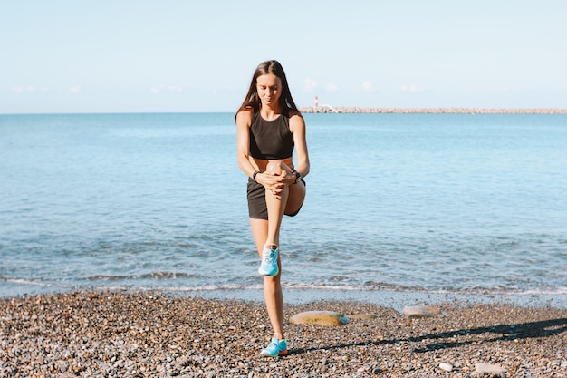 Giovane donna atletica esile in abiti sportivi che fanno gli esercizi sulla spiaggia del mare nella mattina