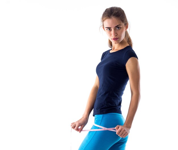 Giovane donna atletica in maglietta blu e leggings che le misurano le natiche con un centimetro in studio