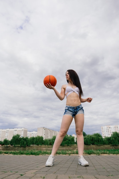 Giovane donna atletica, in un top e pantaloni della tuta, giocando con la palla sul campo da basket all'aperto.