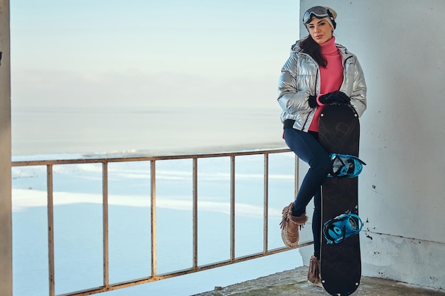 Giovane donna attiva con lo snowboard sta posando per il fotografo in una luminosa giornata invernale.