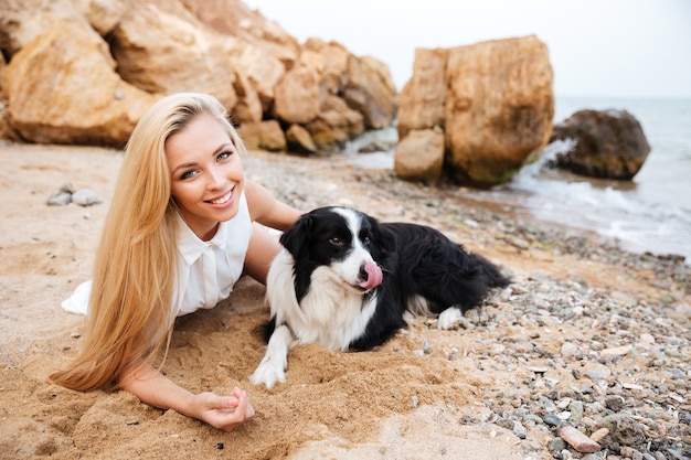 Giovane donna attraente allegra che riposa con il cane sulla spiaggia