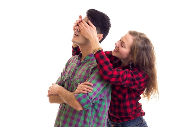 Giovane donna attraente che chiude gli occhi del giovane uomo bello con i capelli scuri in camicia a quadri