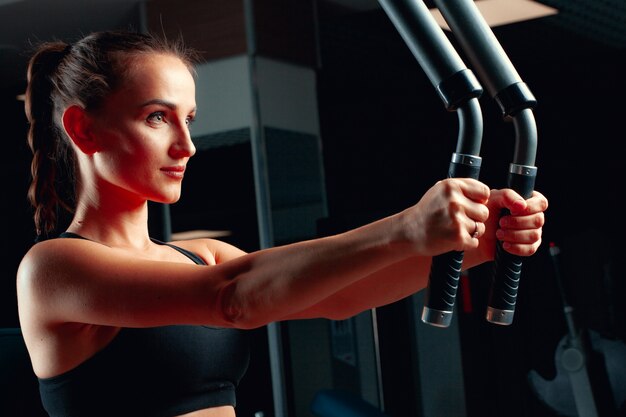 Giovane donna attraente che fa le esercitazioni per le braccia in una macchina di addestramento