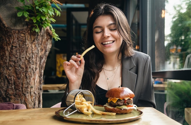 Giovane donna attraente che mangia patatine fritte e un hamburger in un ristorante