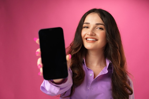Giovane donna attraente che mostra lo schermo in bianco dello smartphone con lo spazio della copia