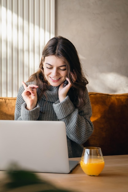 Giovane donna attraente che parla al telefono e che lavora su un computer portatile