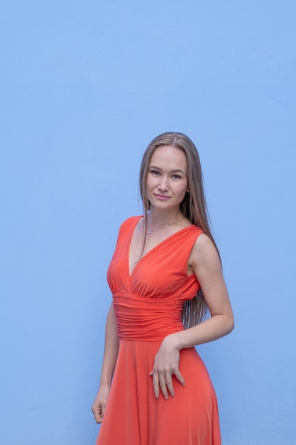 Giovane donna attraente che posa con il vestito rosso in parete blu